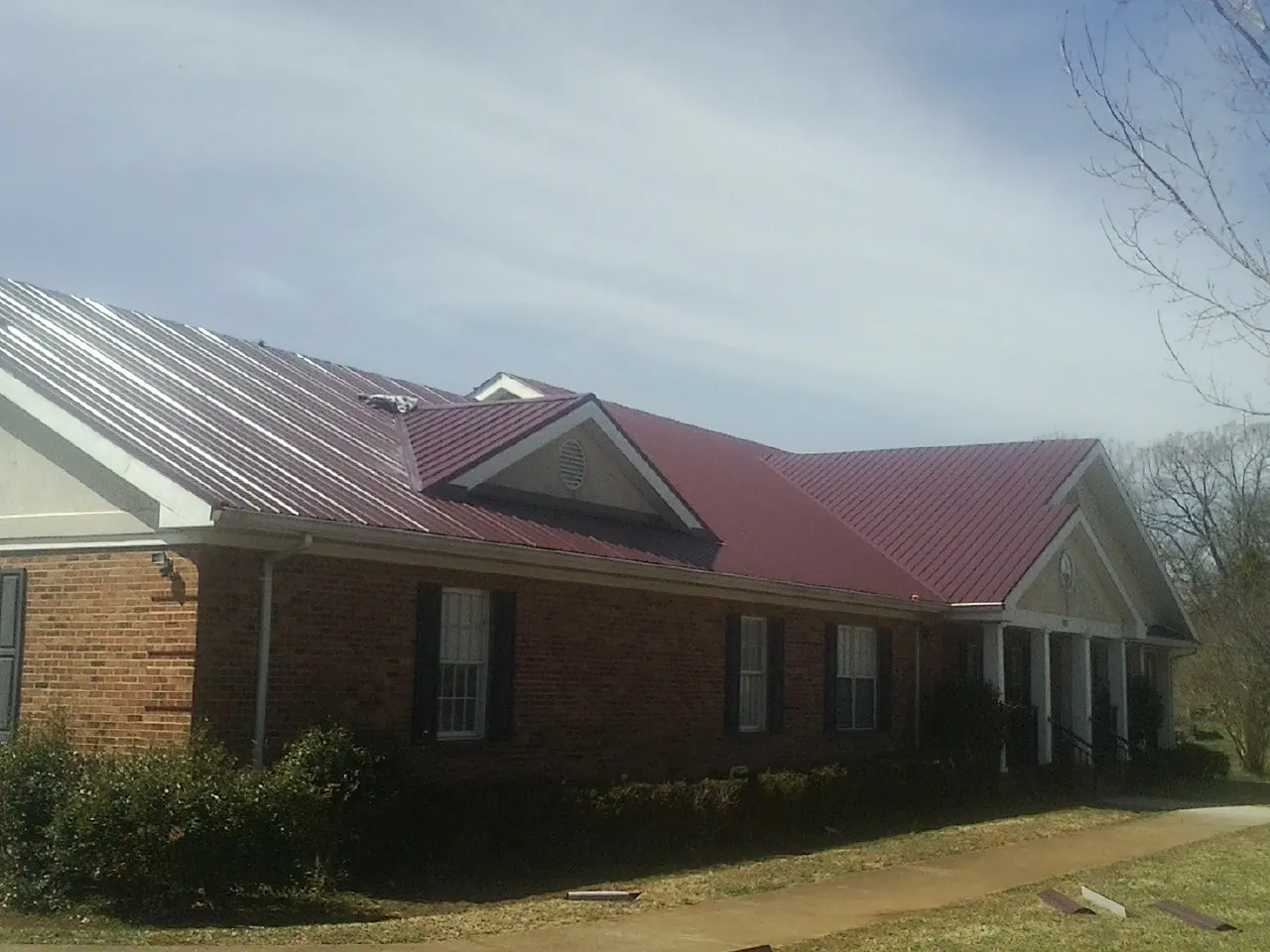 Red metal roof with gabled entries on a long brick building, from a Hail Damage Roof Repair job in Bastrop