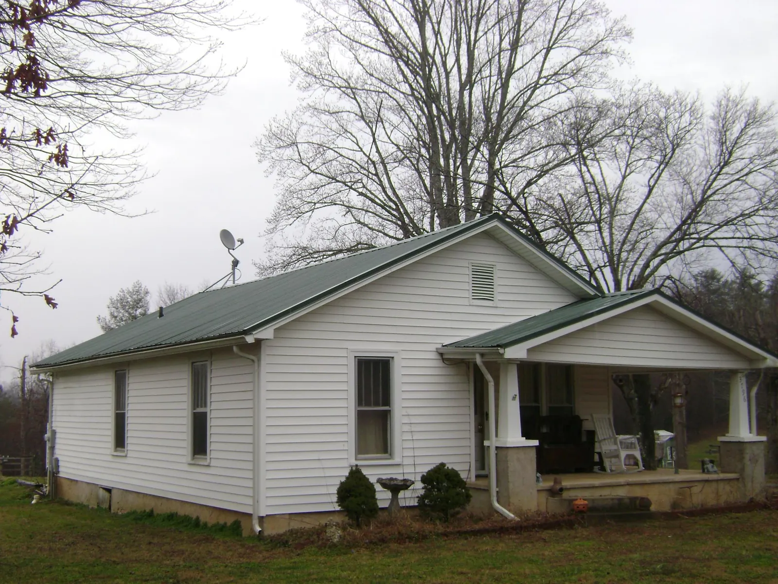 Green metal roof on a white bungalow with a side porch in Bastrop