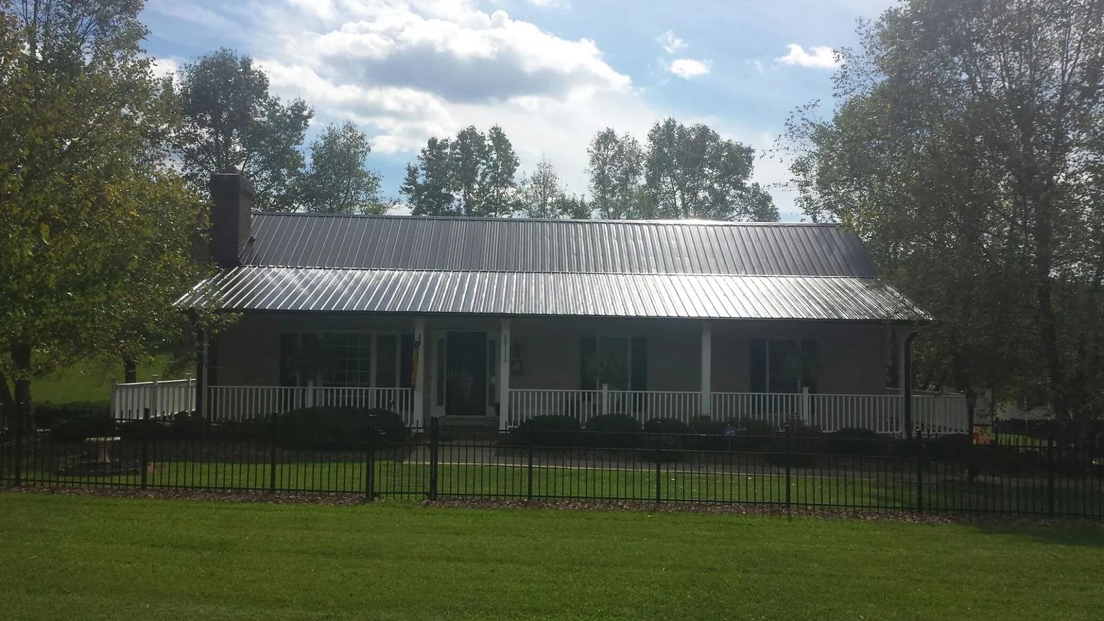 Gray metal roof on a brick ranch with a full width front porch — Gutter Guard Installation work by our crew in Bastrop